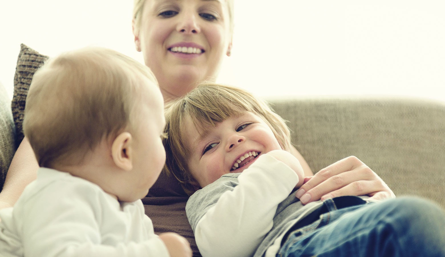 Lachende Mutter mit zwei Kleinkindern im Arm