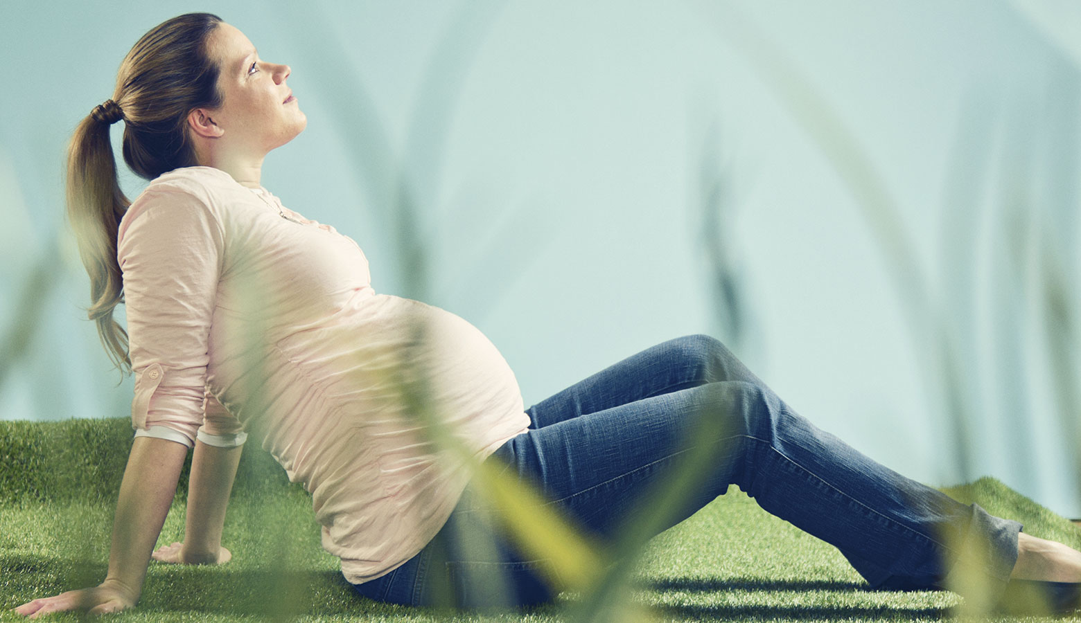 Schwangere auf Gras sitzend, blickt nach oben. 