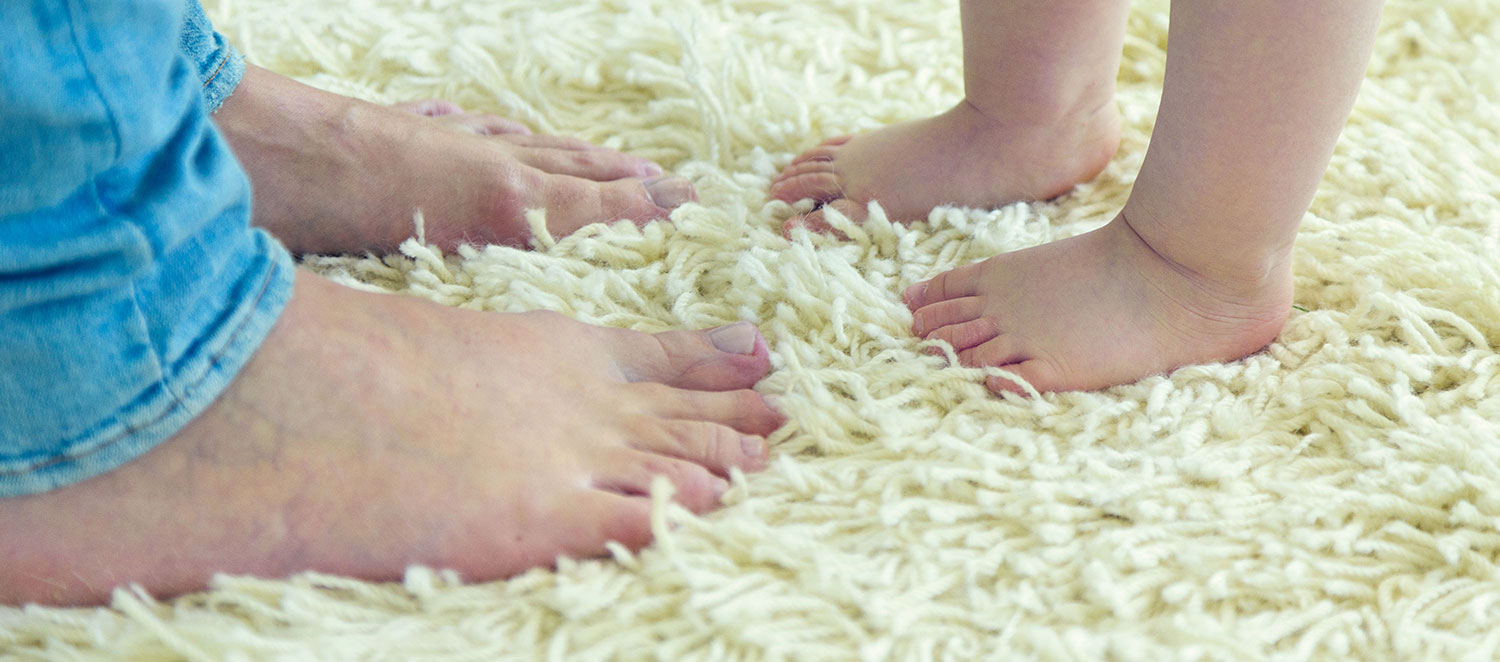 Zwei große Füße stehen zwei kleinen Füßen eines Kindes auf dem Teppich gegenüber. 