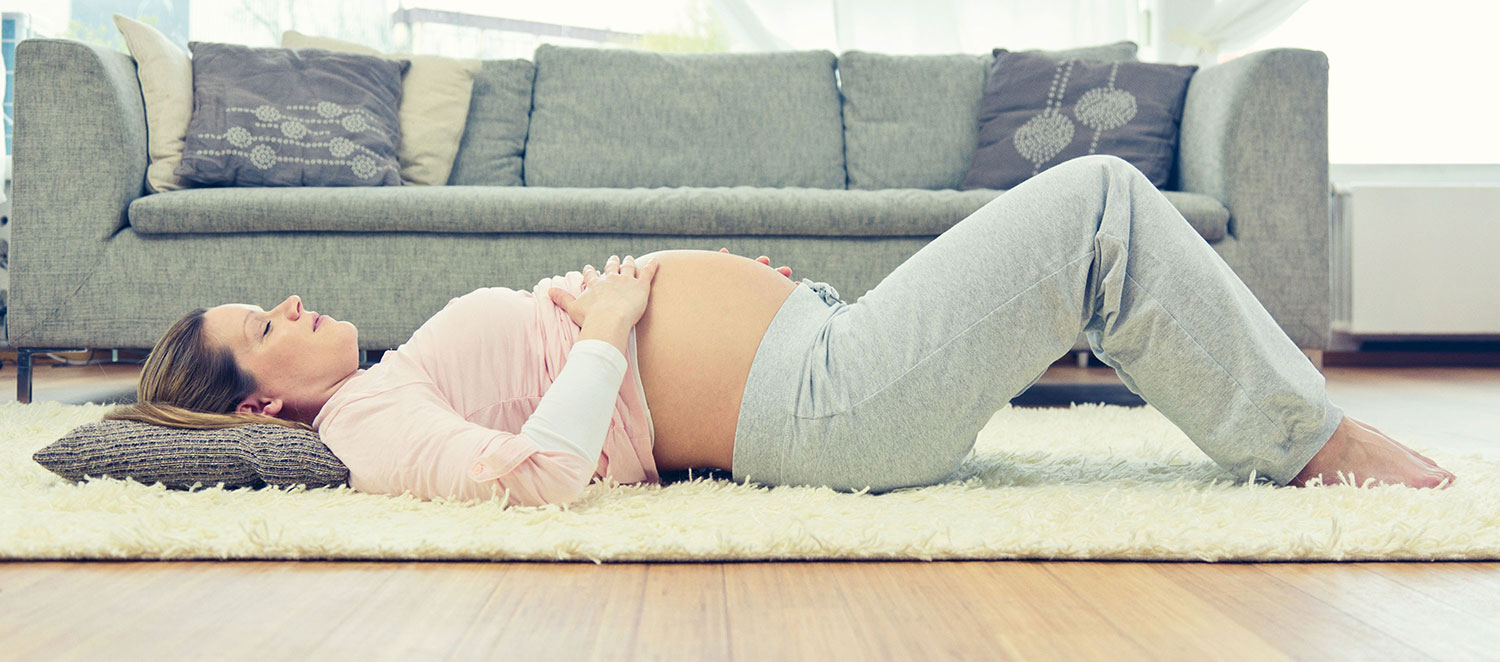 Schwangere Frau liegt auf dem Teppich mit Händen auf nacktem Bauch. 