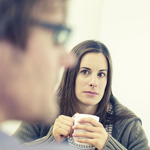 Frau mit Kaffeetasse schaut zu einem Mann. 